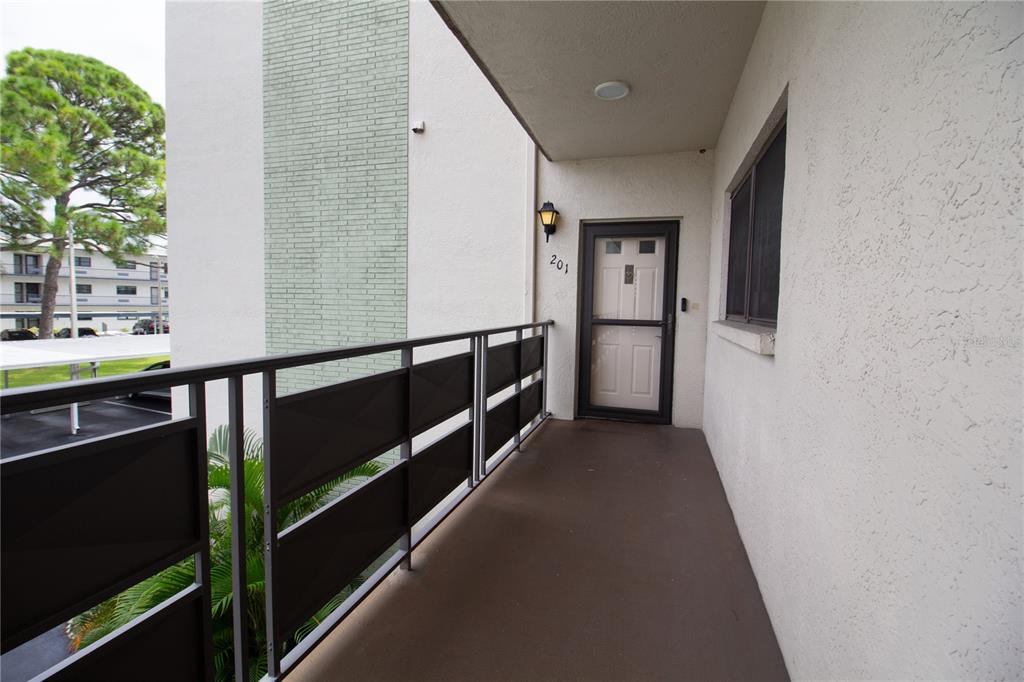 An exterior view of a covered apartment balcony with a metal railing and door 201 — 6080 80TH STREET N UNIT 201, ST PETERSBURG, FL