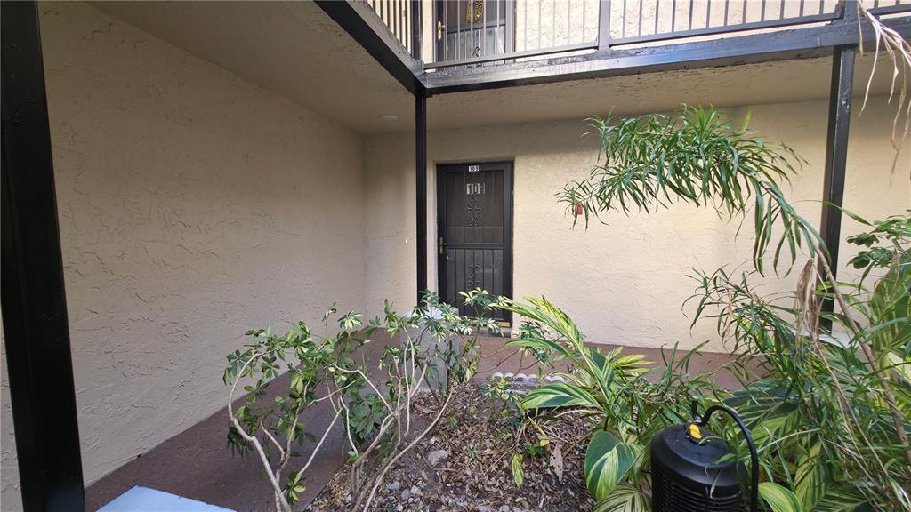 A ground-level apartment entrance features a dark metal screen door and surrounding landscaping — 2025 SYLVESTER ROAD UNIT N109, LAKELAND, FL