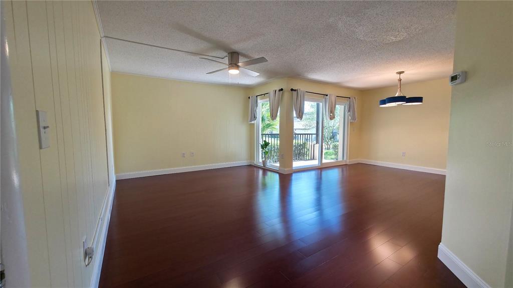 An empty living room features yellow walls, dark wood flooring, and a sliding glass door — 2025 SYLVESTER ROAD UNIT N109, LAKELAND, FL