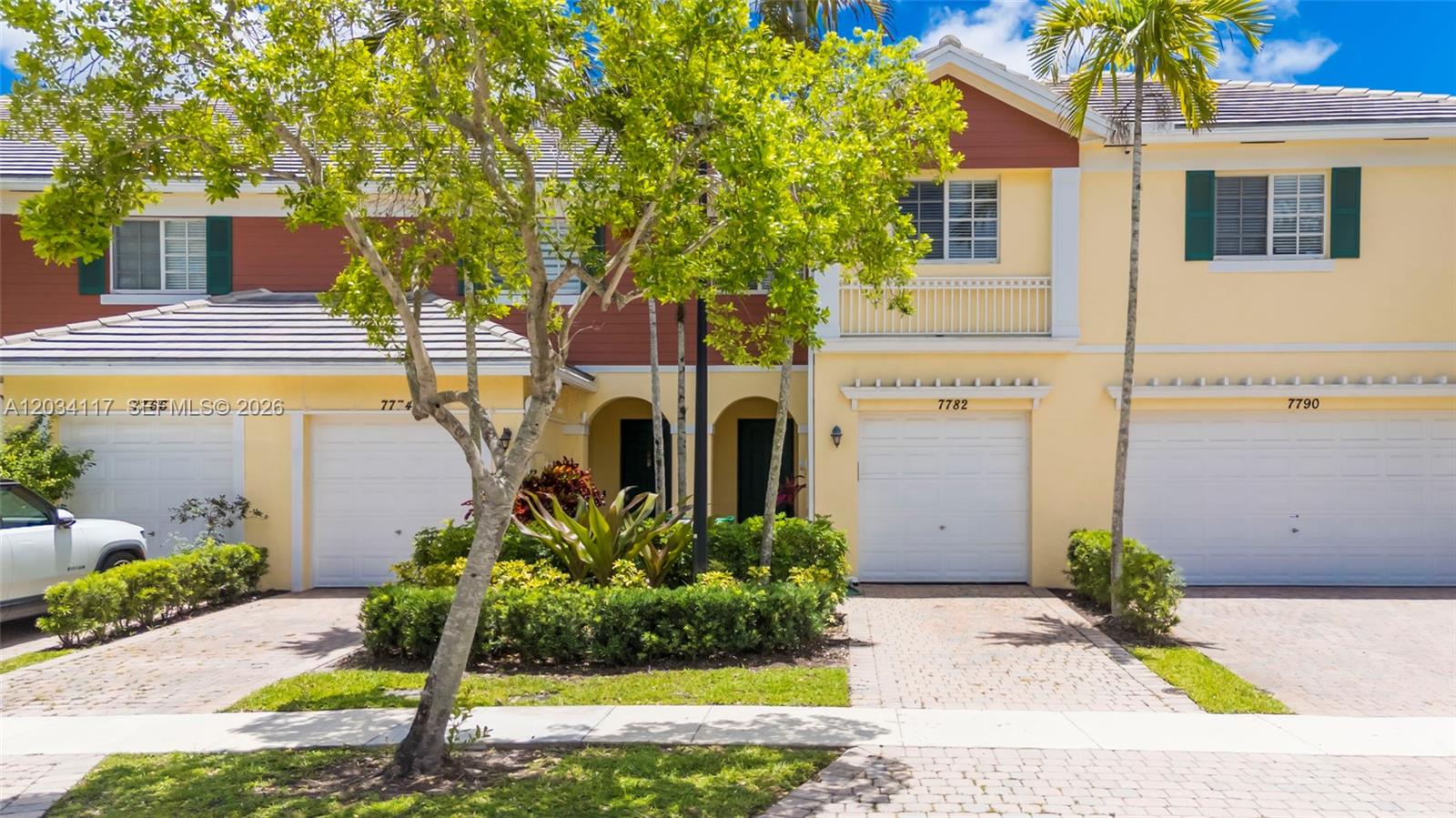 A row of yellow townhouses features white garage doors, arched entryways, and palm trees — 7782 Paddock Pl, Davie FL 33328, DAVIE, FL