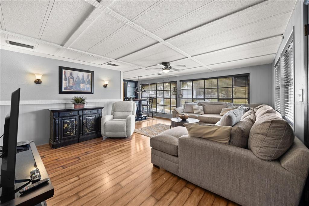 A living room features light gray walls, wood-look flooring, a sectional sofa, and a ceiling fan — 2129 OAK GROVE DRIVE UNIT 58, ZELLWOOD, FL
