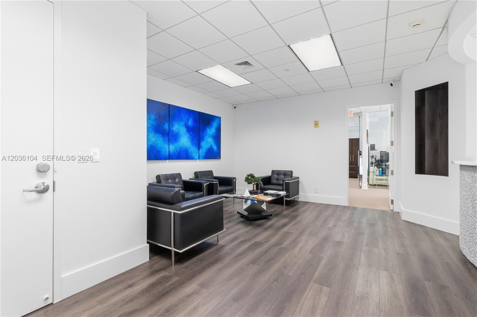 A waiting room features black leather chairs, a glass coffee table, and blue wall art — 175 SW 7th St # 1612, Miami FL 33130, MIAMI, FL