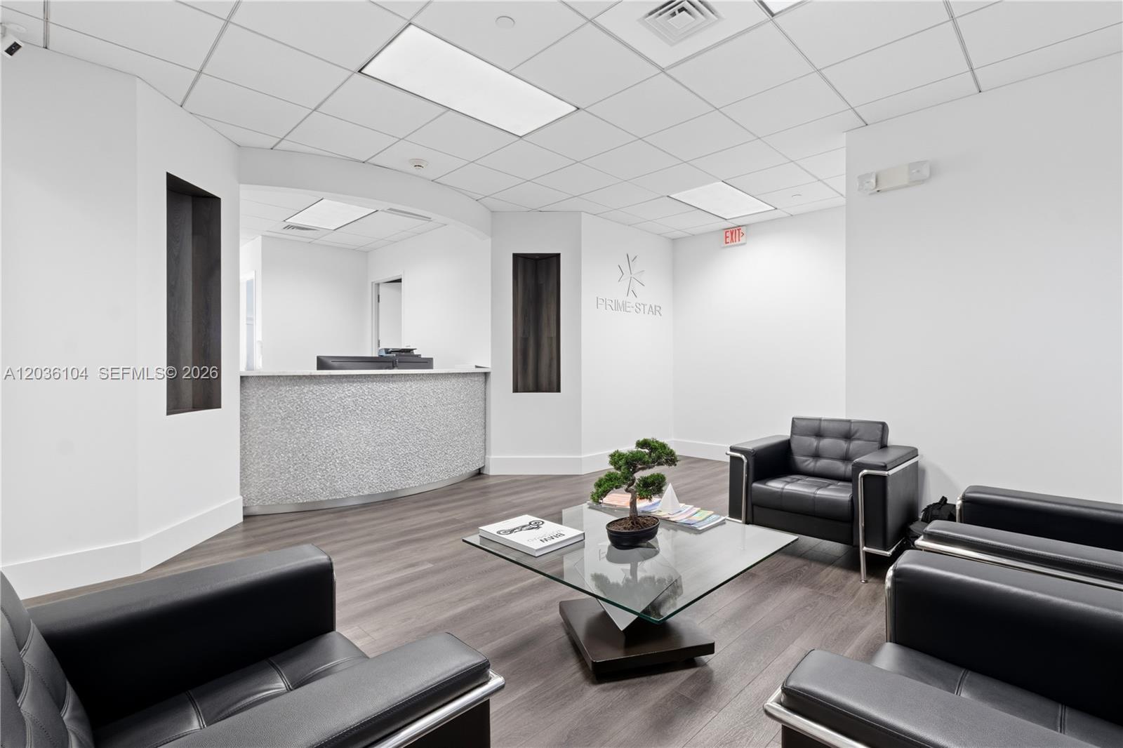 A modern office reception area features a curved desk, black leather chairs, and wood flooring — 175 SW 7th St # 1612, Miami FL 33130, MIAMI, FL