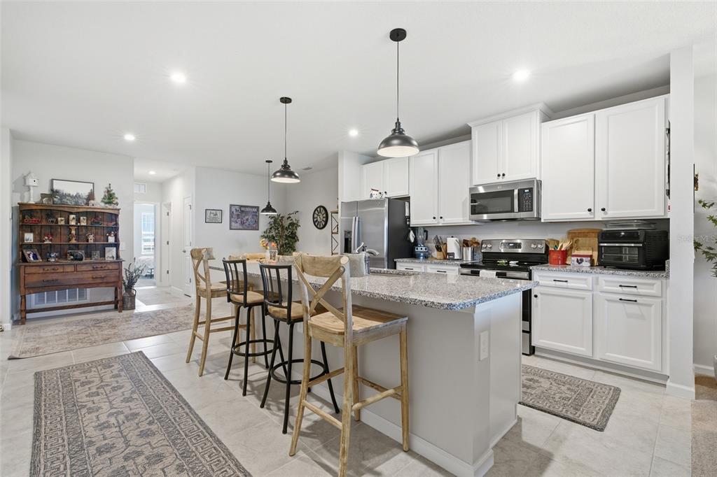 A kitchen features white cabinets, granite countertops, a central island with bar stools, and lighting — 16300 COCONUT PALM DRIVE, PORT CHARLOTTE, FL