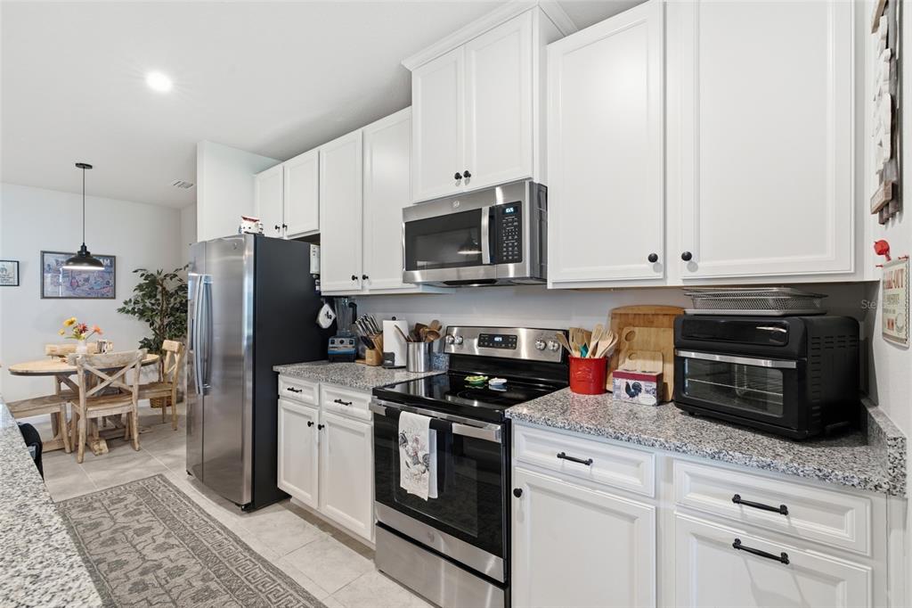A kitchen features white cabinets, granite countertops, stainless steel appliances, and an adjacent dining area — 16300 COCONUT PALM DRIVE, PORT CHARLOTTE, FL