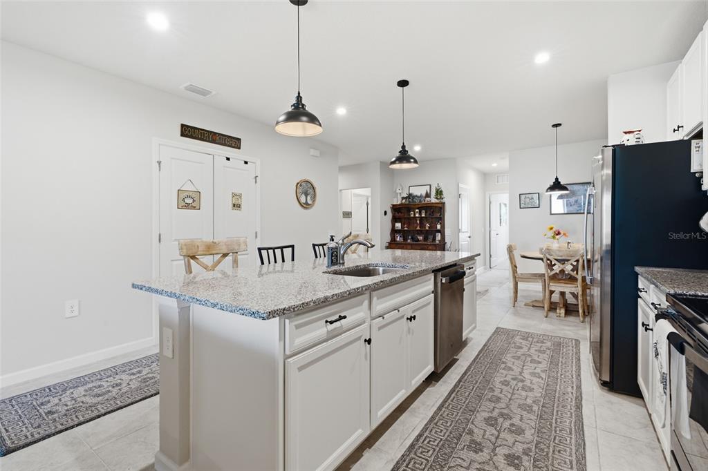 A kitchen features a granite-topped island, white cabinetry, stainless steel appliances, and pendant lighting — 16300 COCONUT PALM DRIVE, PORT CHARLOTTE, FL