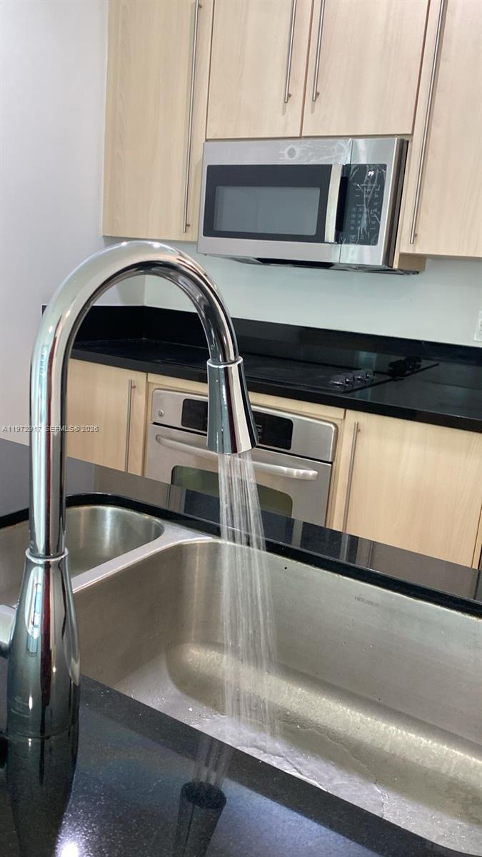 A kitchen features light wood cabinets, black countertops, stainless steel appliances, and a chrome faucet — 1111 SW 1st Ave, Miami FL 33130, MIAMI, FL