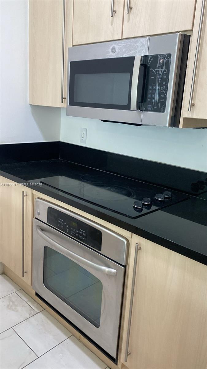 A kitchen features light wood cabinets, a black countertop, and stainless steel appliances — 1111 SW 1st Ave, Miami FL 33130, MIAMI, FL
