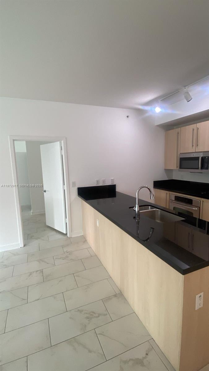 A kitchen features light wood cabinets, black countertops, and light-colored tile flooring — 1111 SW 1st Ave, Miami FL 33130, MIAMI, FL