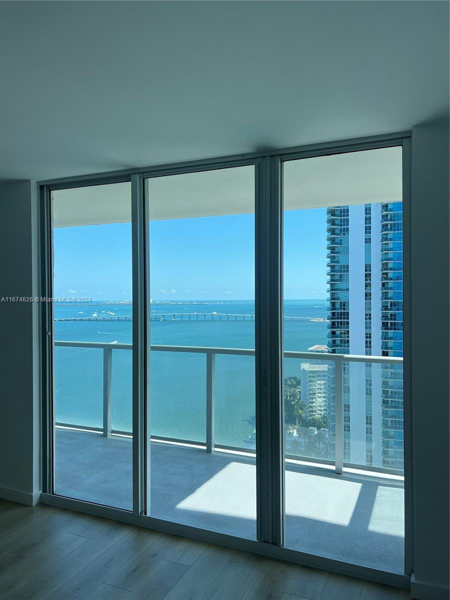 A room with floor-to-ceiling glass sliding doors overlooking a balcony, the ocean, and a bridge — 1155 Brickell Bay Dr # 3205, Miami FL 33131, MIAMI, FL