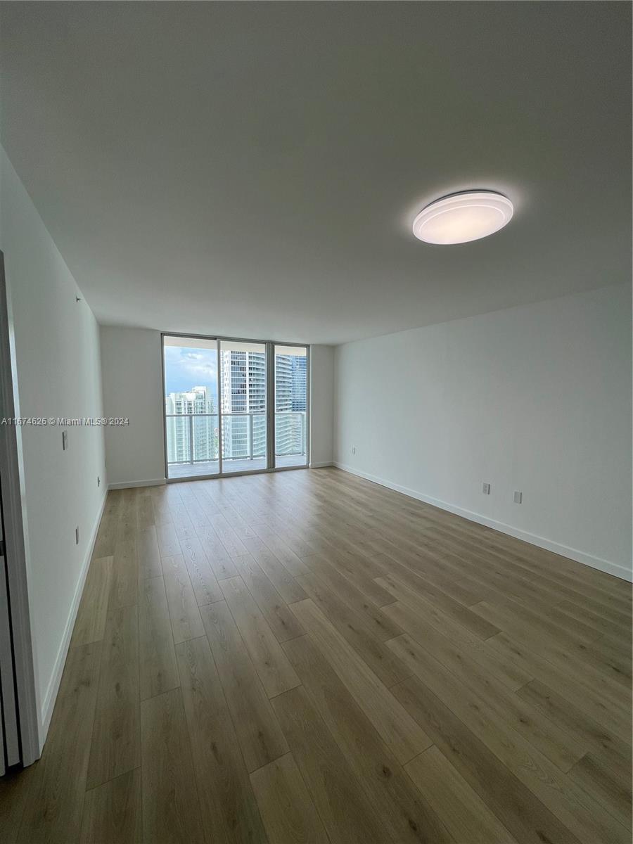 An empty room features light wood-look flooring, white walls, a flush-mount ceiling light, and balcony access — 1155 Brickell Bay Dr # 3205, Miami FL 33131, MIAMI, FL