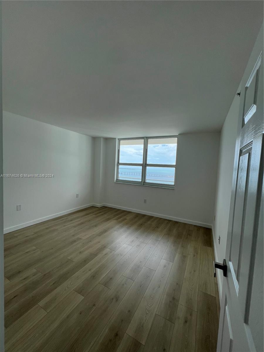 An empty room features light wood-look flooring, white walls, and a window overlooking the ocean — 1155 Brickell Bay Dr # 3205, Miami FL 33131, MIAMI, FL