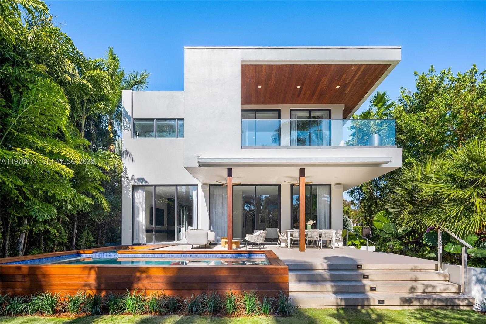 A modern two-story house features a wooden deck, a swimming pool, and a covered patio — 5701 N Bay Rd, Miami Beach FL 33140, MIAMI BEACH, FL