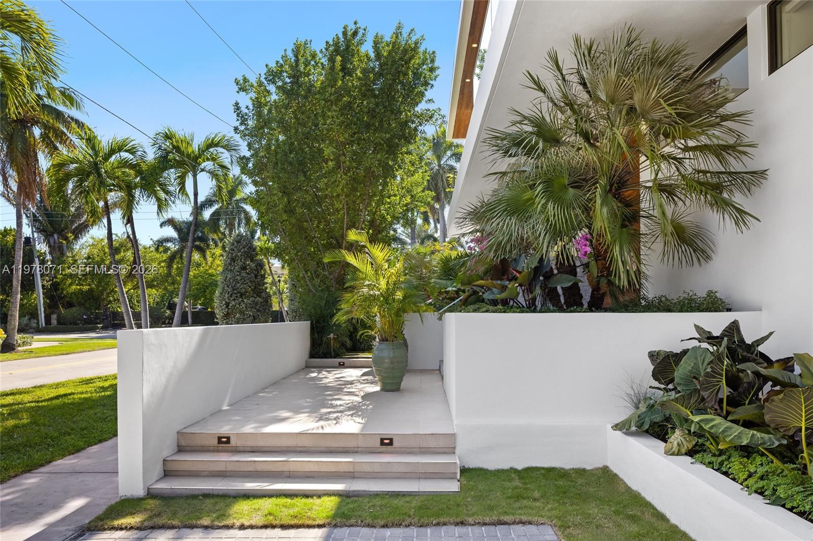 A modern home exterior features a white concrete staircase leading to a landscaped entrance area — 5701 N Bay Rd, Miami Beach FL 33140, MIAMI BEACH, FL