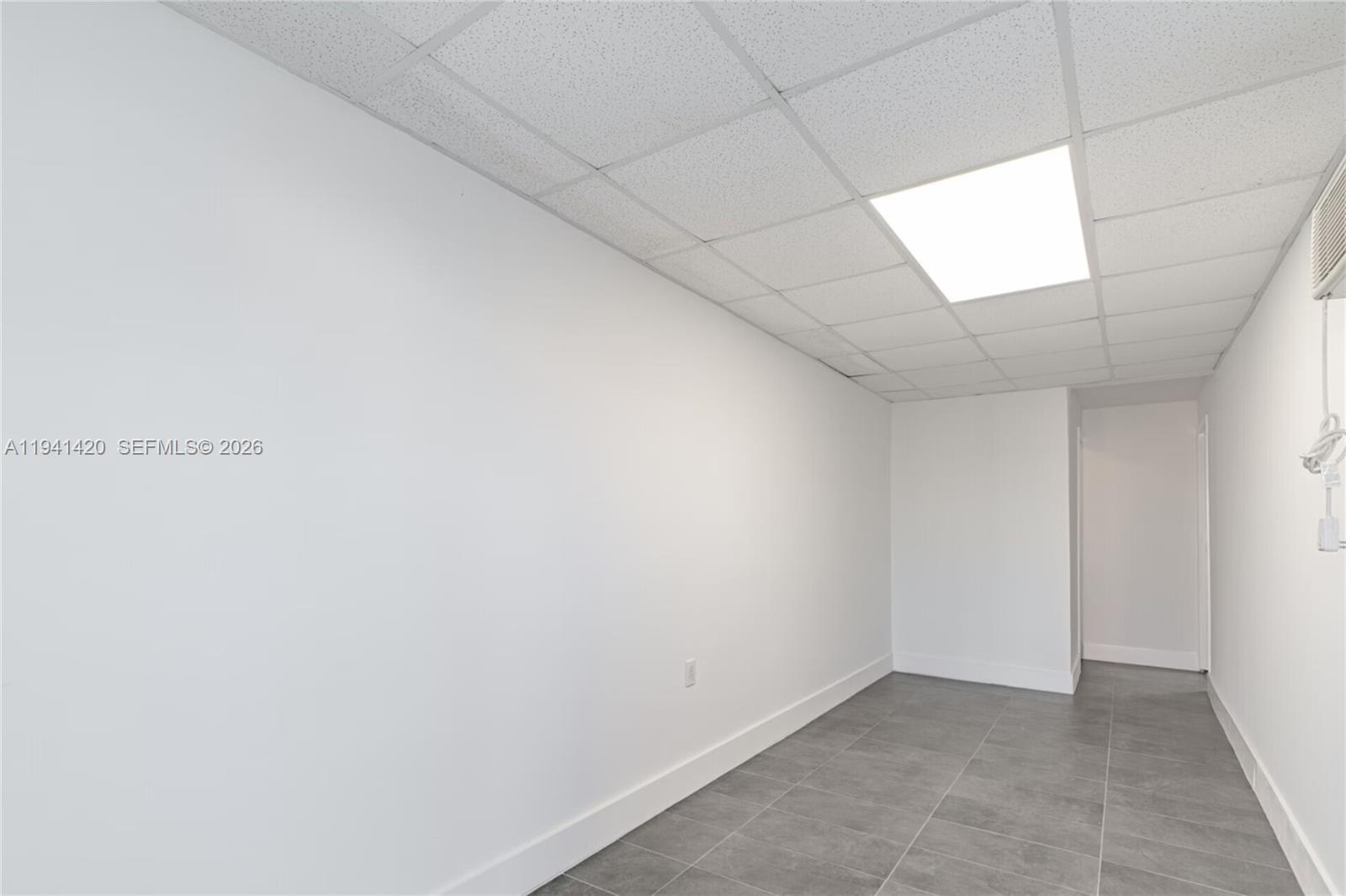 A small, empty room features white walls, gray tile flooring, and a drop ceiling — 726 W 28th St, Hialeah FL 33010, HIALEAH, FL