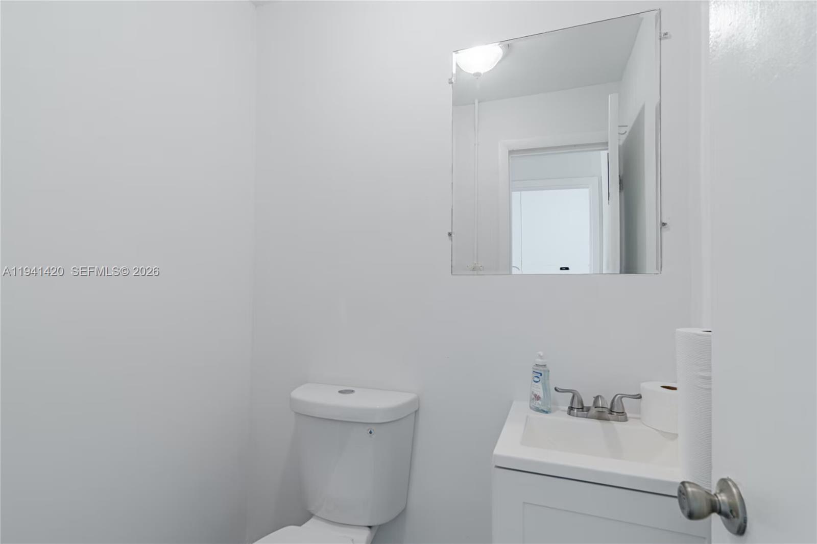 A small, white-walled bathroom features a toilet, a vanity with a sink, and a mirror — 726 W 28th St, Hialeah FL 33010, HIALEAH, FL