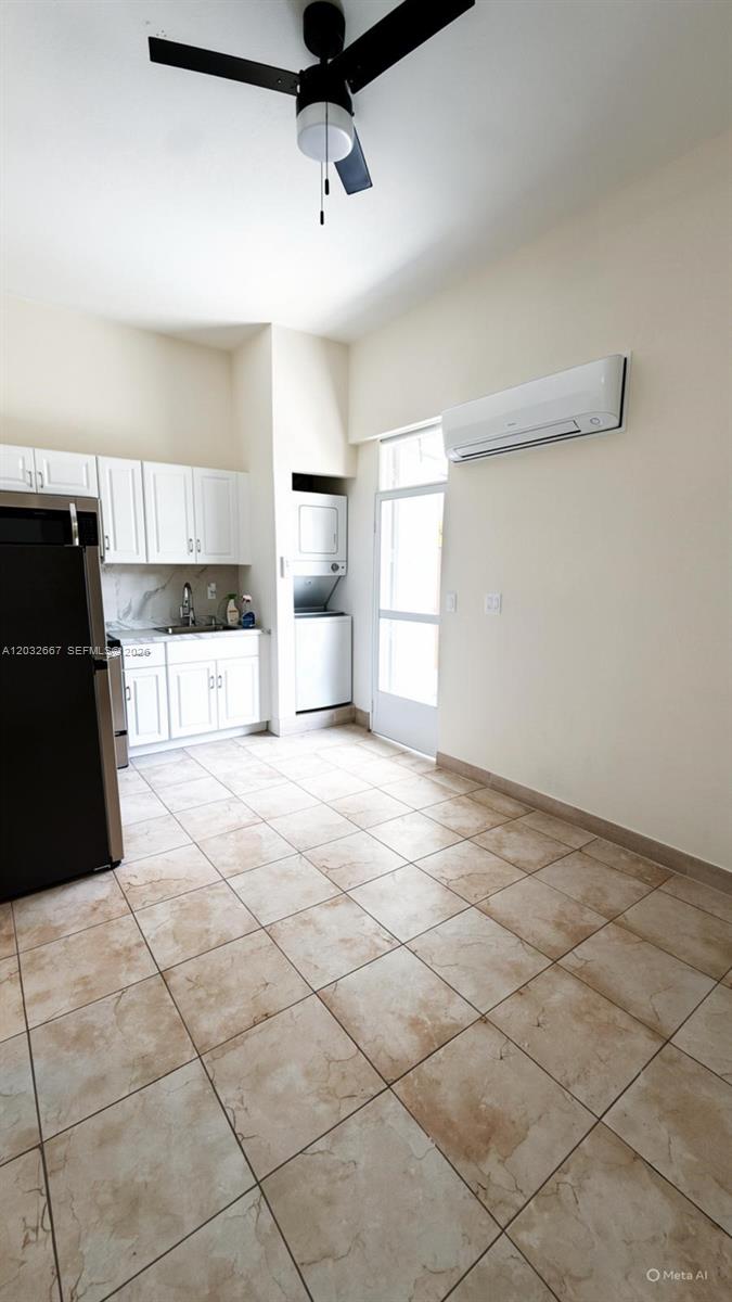 A kitchen features white cabinets, a black refrigerator, a stacked washer-dryer, and tile flooring — 18405 SW 132nd Ave # 18405, Miami FL 33177, MIAMI, FL