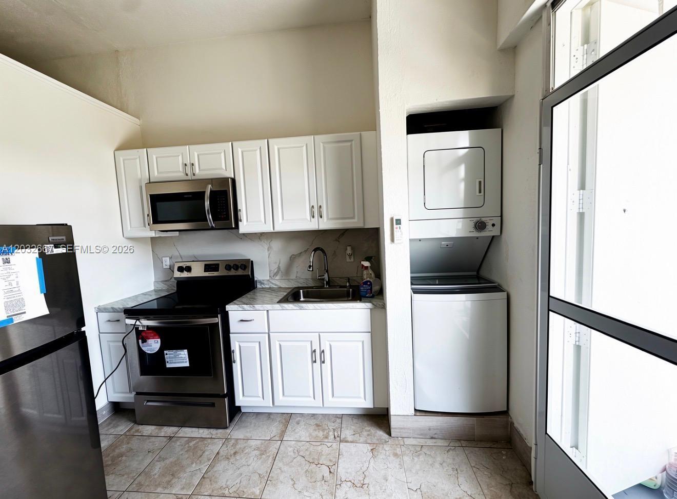 A kitchen features white cabinets, stainless steel appliances, a stacked washer-dryer, and tile flooring — 18405 SW 132nd Ave # 18405, Miami FL 33177, MIAMI, FL