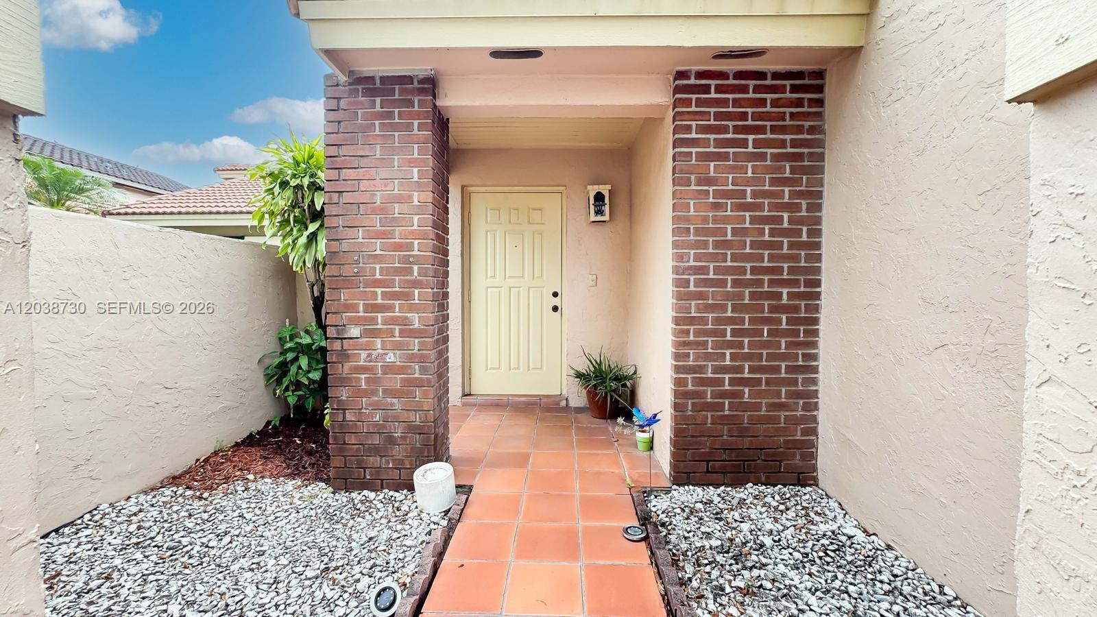 An exterior view of a home entrance featuring a brick-columned porch and a yellow door — 6320 NW 173rd St, Hialeah FL 33015, HIALEAH, FL