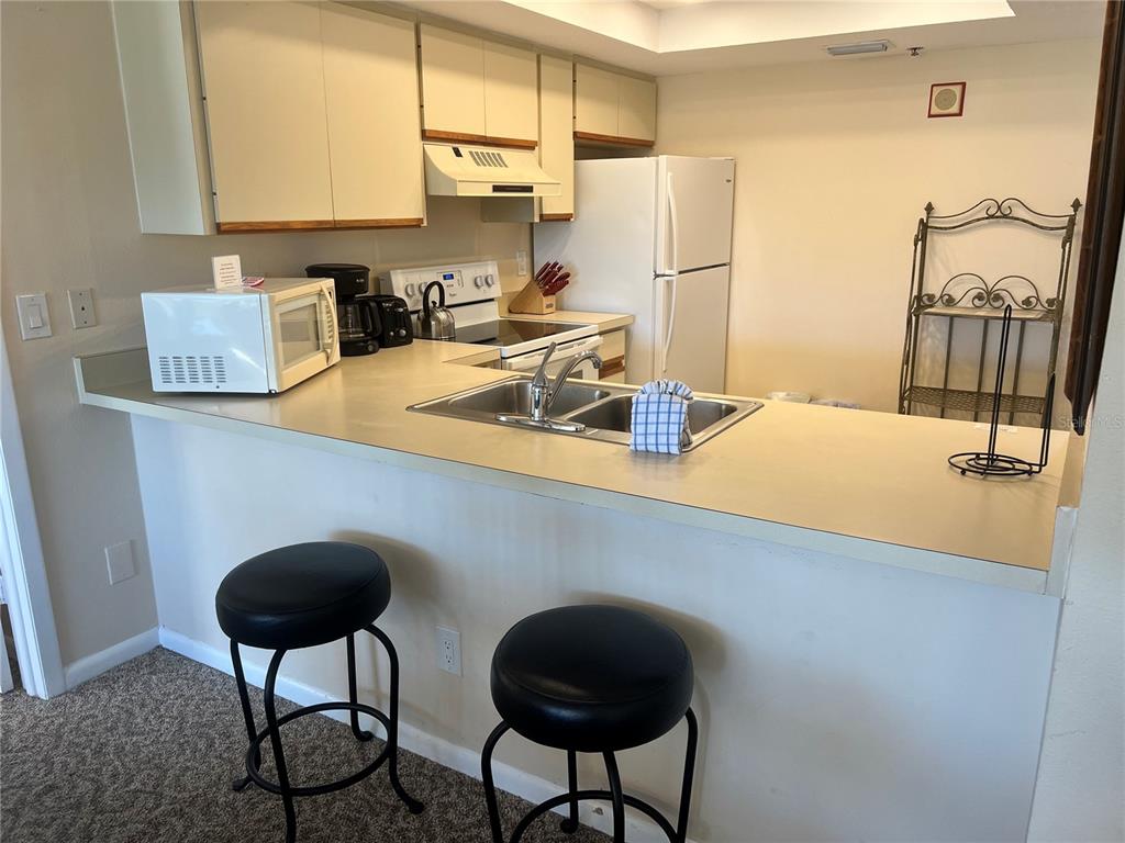 A kitchen features a breakfast bar with two black stools, white cabinets, and white appliances — 1001 POINT OF ROCKS ROAD UNIT 309, SARASOTA, FL