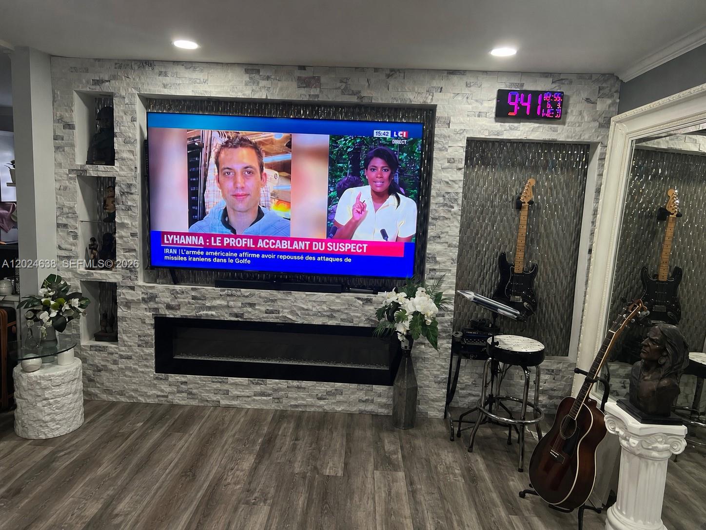 A living room features a stone-accented wall with a fireplace, television, and musical instruments — 5300 Washington St # H140, Hollywood FL 33021, HOLLYWOOD, FL