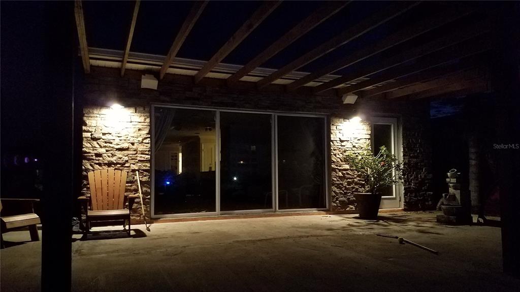 A covered patio at night features a stone wall, sliding glass doors, and wooden beams — 4457 FLORAMAR TERRACE, NEW PORT RICHEY, FL