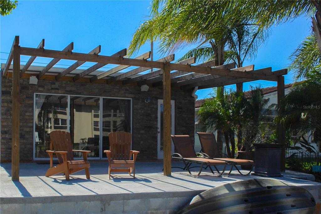 A stone-walled patio features a wooden pergola, two Adirondack chairs, and two lounge chairs — 4457 FLORAMAR TERRACE, NEW PORT RICHEY, FL
