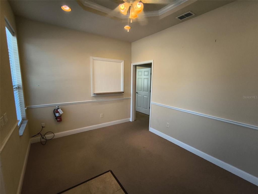 An office room features beige walls, a white whiteboard, a fire extinguisher, and carpeted flooring — 4875 PALM COAST PARKWAY NW UNIT 4, PALM COAST, FL