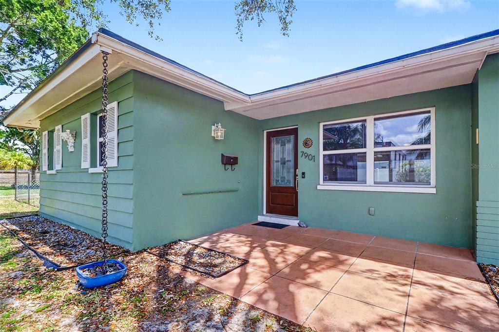 The exterior of a green house features a tiled front porch and a rain chain — 7901 3RD STREET N, ST PETERSBURG, FL