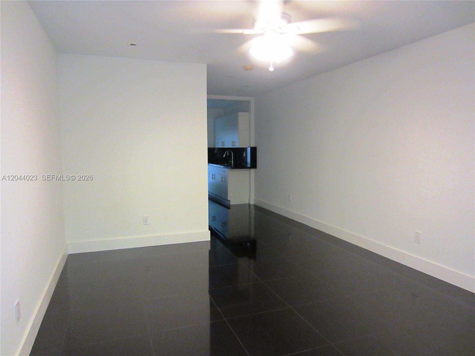 A room with white walls and black tile flooring leads to a kitchen area — 8132 Harding Ave # 5, Miami Beach FL 33141, MIAMI BEACH, FL