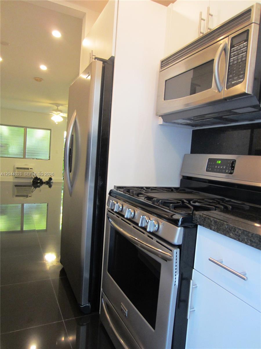 A kitchen features stainless steel appliances, white cabinets, and dark tile flooring — 8132 Harding Ave # 5, Miami Beach FL 33141, MIAMI BEACH, FL