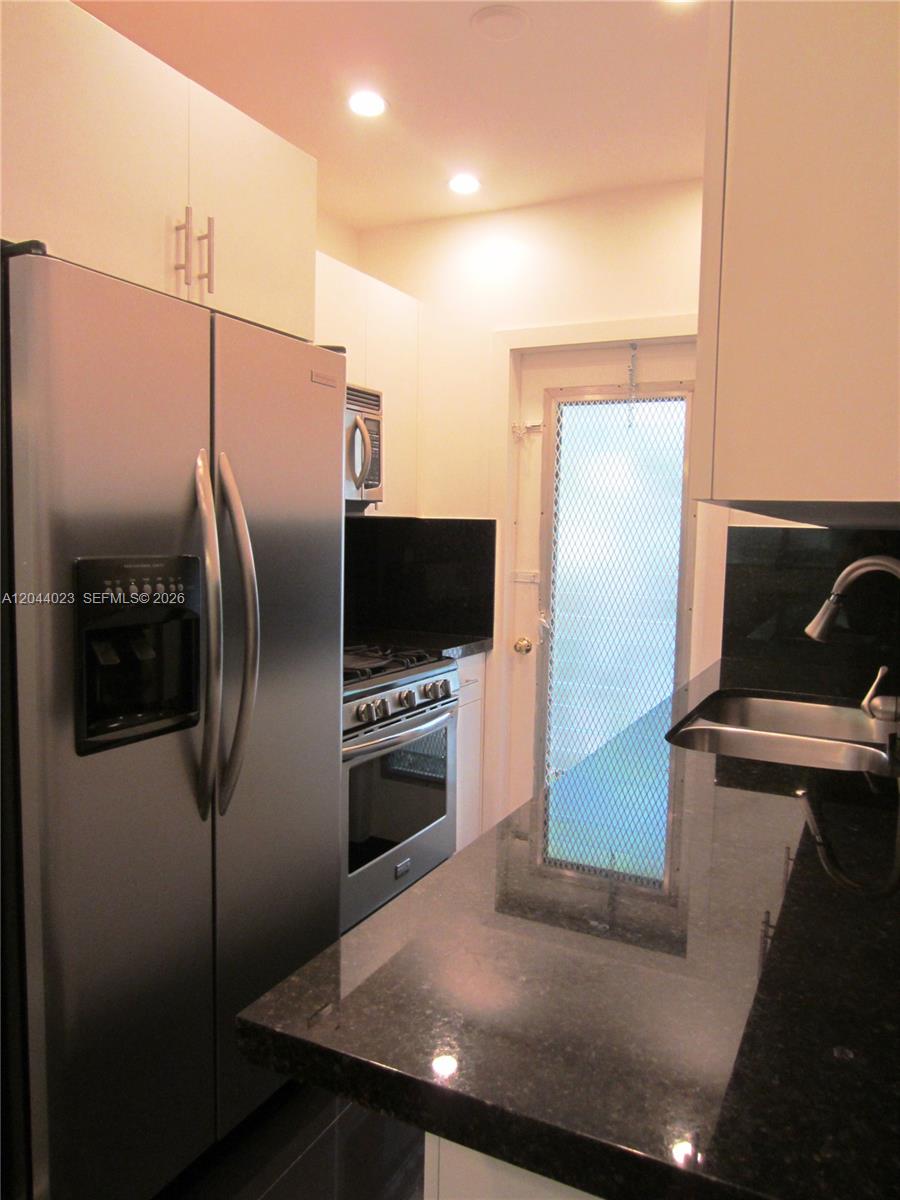 A kitchen features stainless steel appliances, white cabinetry, and black granite countertops — 8132 Harding Ave # 5, Miami Beach FL 33141, MIAMI BEACH, FL