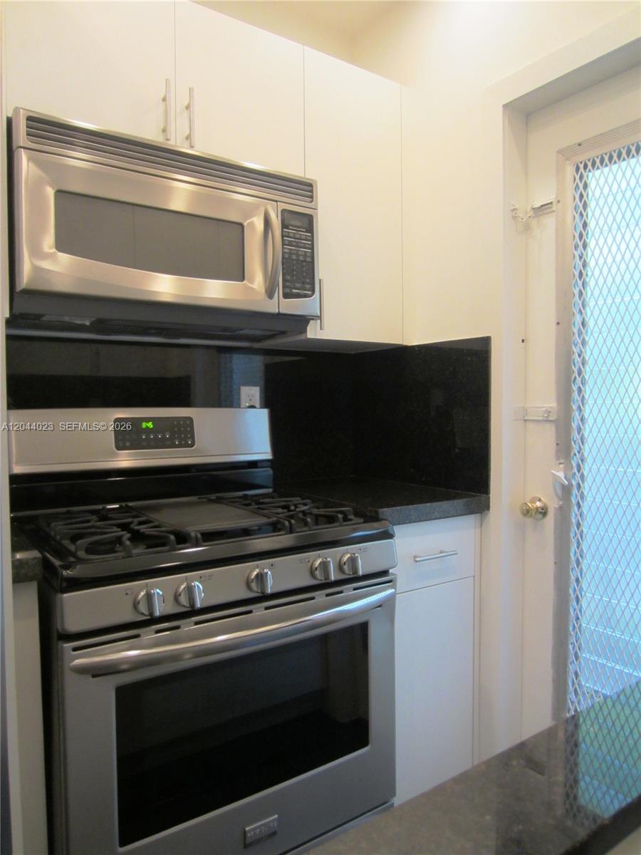 A kitchen features stainless steel appliances, white cabinetry, and black granite countertops — 8132 Harding Ave # 5, Miami Beach FL 33141, MIAMI BEACH, FL