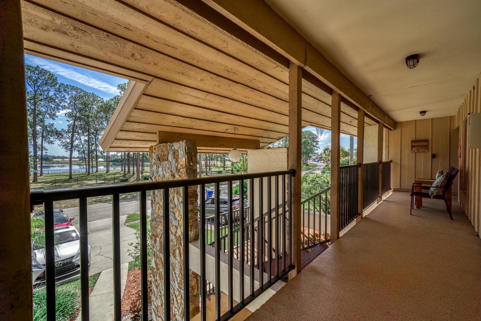 A covered balcony with a stone pillar, black metal railing, and a view of trees — 3833 Edgewater Drive, Sebring FL 33872, SEBRING, FL