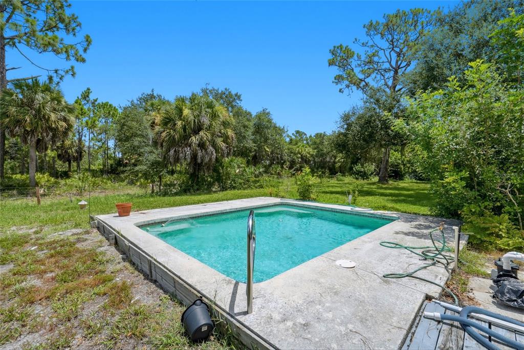 An outdoor rectangular swimming pool is surrounded by a concrete deck and a grassy yard — 427 RUBENS DRIVE, NOKOMIS, FL