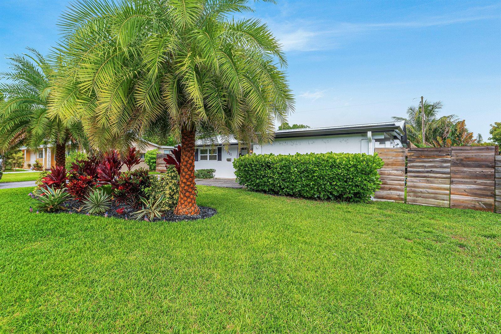 A single-story house with a palm tree, landscaping, and a wooden fence in the yard — 711 Laurel Drive, Lake Park FL 33403, LAKE PARK, FL