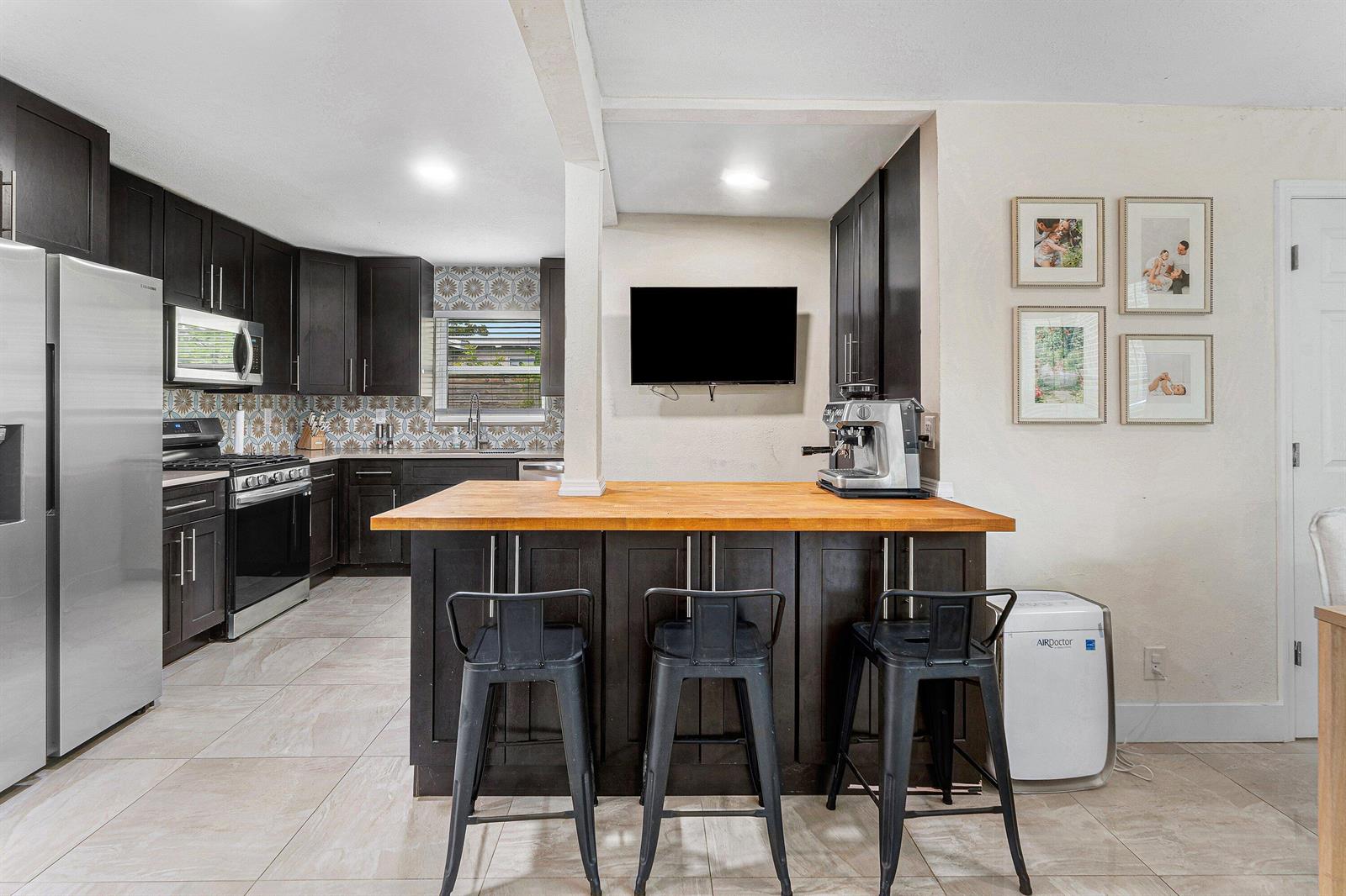 A kitchen features dark cabinetry, a wooden island with bar stools, and stainless steel appliances — 711 Laurel Drive, Lake Park FL 33403, LAKE PARK, FL