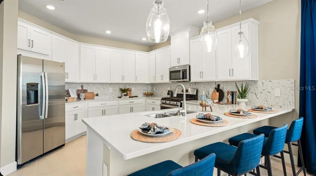 A kitchen with white cabinets, stainless steel appliances, a quartz island, and blue bar stools — 823 STEEL DRIVE, APOLLO BEACH, FL