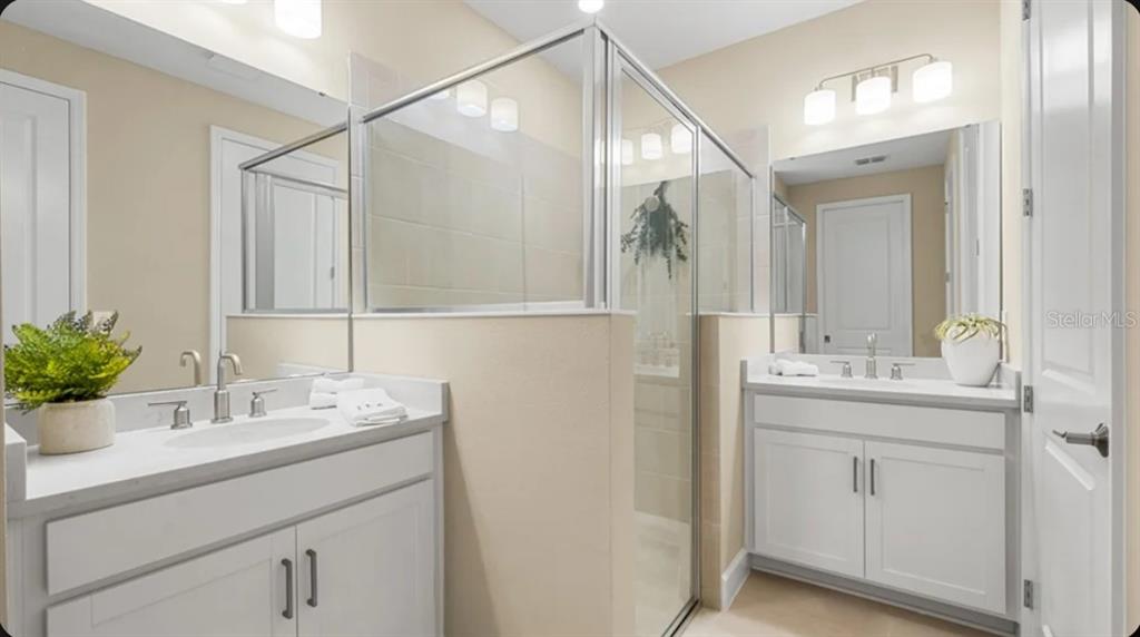 A bathroom features two white vanities with sinks, a glass-enclosed shower, and neutral wall paint — 823 STEEL DRIVE, APOLLO BEACH, FL