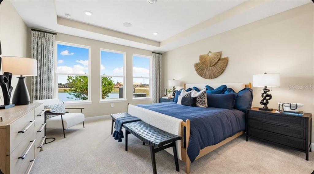 A bedroom features a king bed with blue bedding, a bench, and large windows overlooking water — 823 STEEL DRIVE, APOLLO BEACH, FL