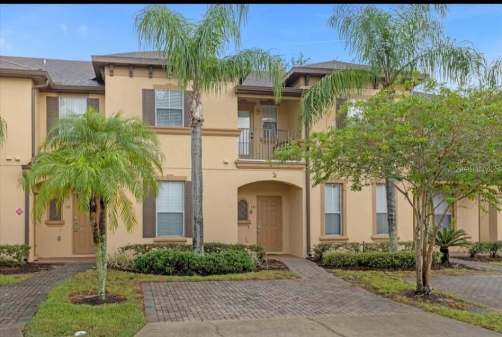 A two-story tan stucco townhouse with a balcony, palm trees, and a brick paver walkway — 216 CALABRIA AVENUE, DAVENPORT, FL