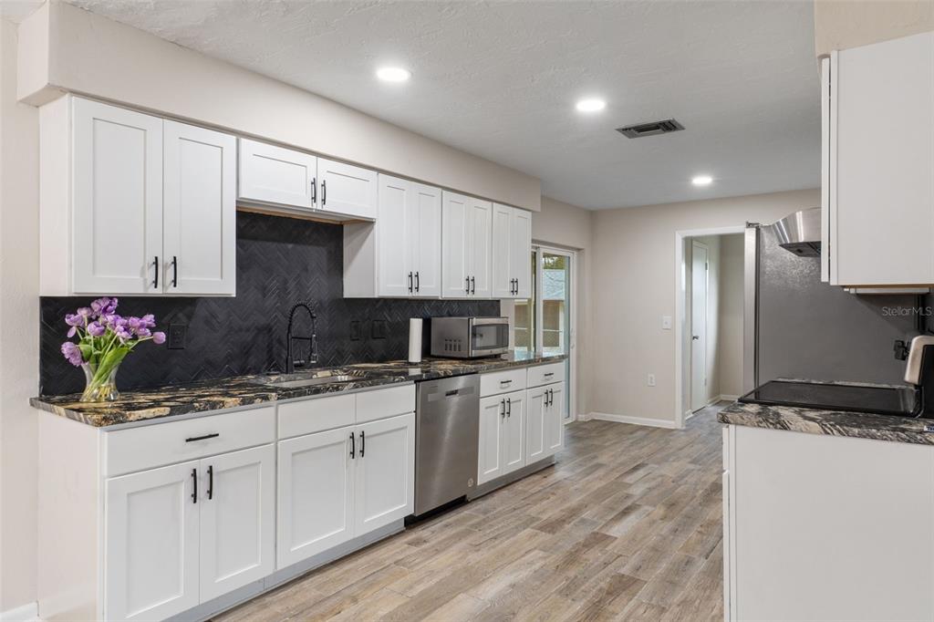 A kitchen with white cabinets, dark patterned countertops, a black herringbone backsplash, and wood-look flooring — 211 S DAVIS STREET, BEVERLY HILLS, FL