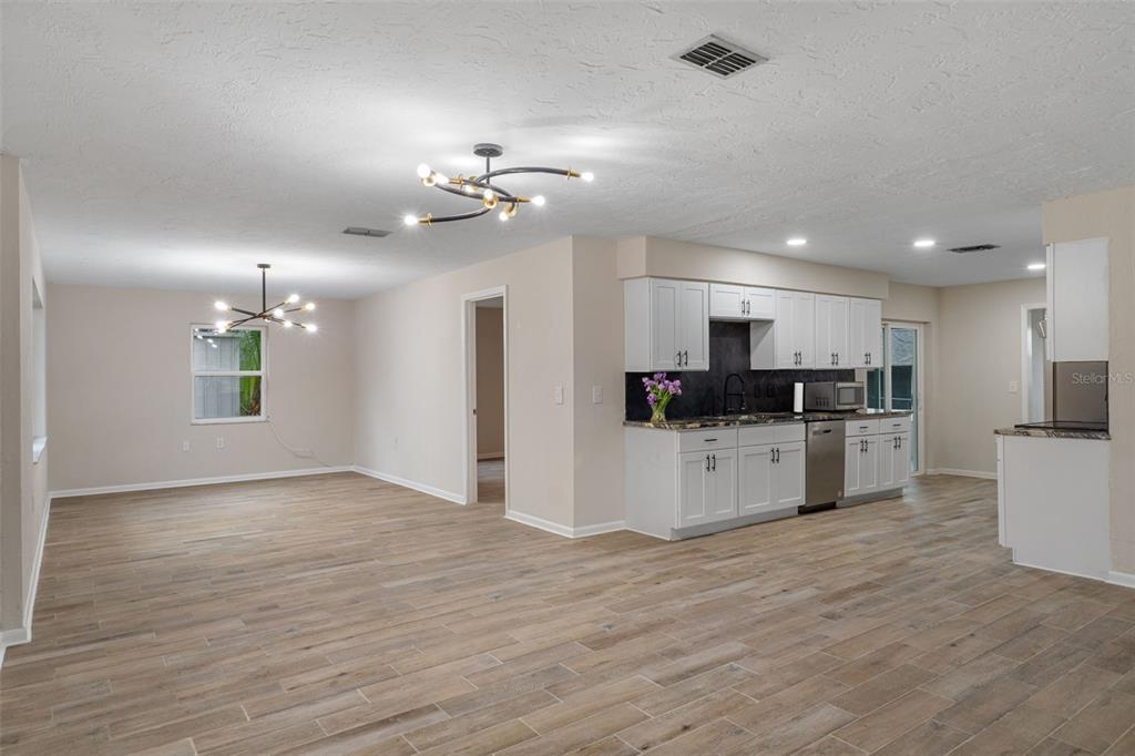 An open-concept kitchen and dining area features white cabinets, dark countertops, and light wood-look flooring — 211 S DAVIS STREET, BEVERLY HILLS, FL
