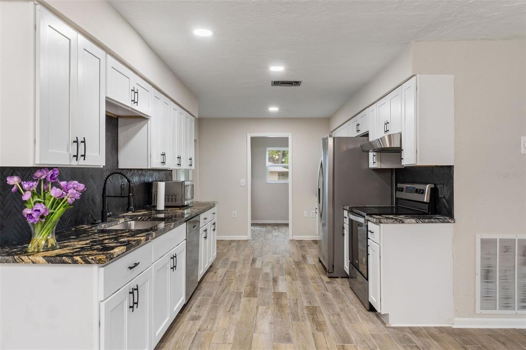 A galley kitchen features white cabinets, black countertops, a dark backsplash, and wood-look tile flooring — 211 S DAVIS STREET, BEVERLY HILLS, FL