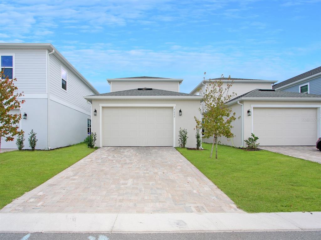 A single-family home exterior features a beige garage, a paver driveway, and green lawns — 2022 EDUCATION STREET, ST CLOUD, FL