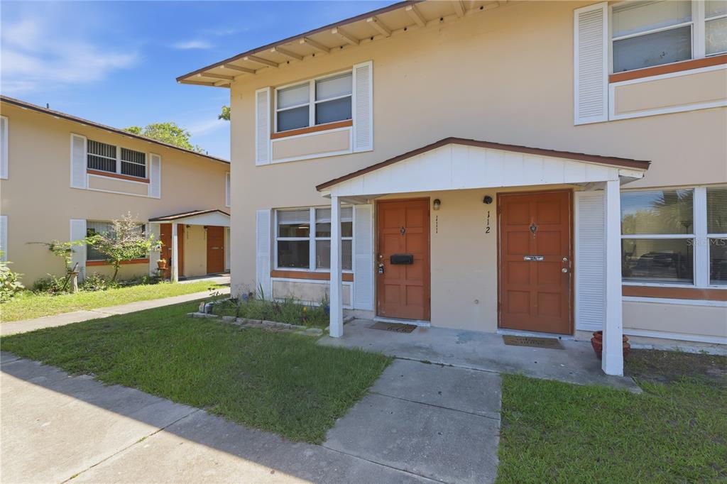 A two-story apartment building features tan stucco walls, brown doors, and a small covered porch — 1600 S PALMETTO AVENUE UNIT 111, SOUTH DAYTONA, FL