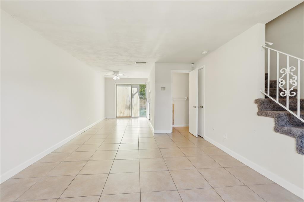 An empty room with light-colored tile flooring, white walls, and a staircase with decorative railings — 1600 S PALMETTO AVENUE UNIT 111, SOUTH DAYTONA, FL