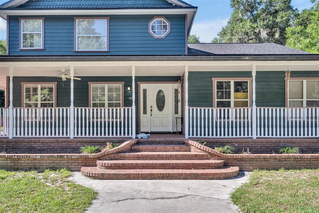 A two-story blue house with a wrap-around porch and brick steps sits on a lawn — 1483 MIRKWOOD COVE, OVIEDO, FL