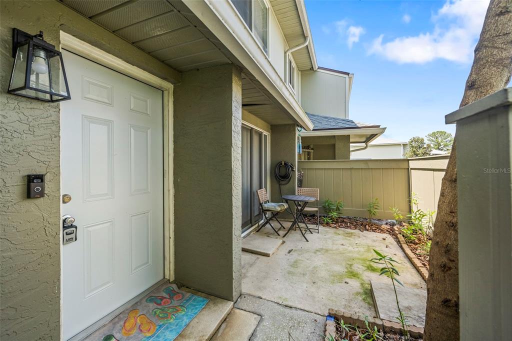 A white front door opens onto a concrete patio with a small bistro set — 4586 PHEASANT RUN DRIVE UNIT 6B, ORLANDO, FL