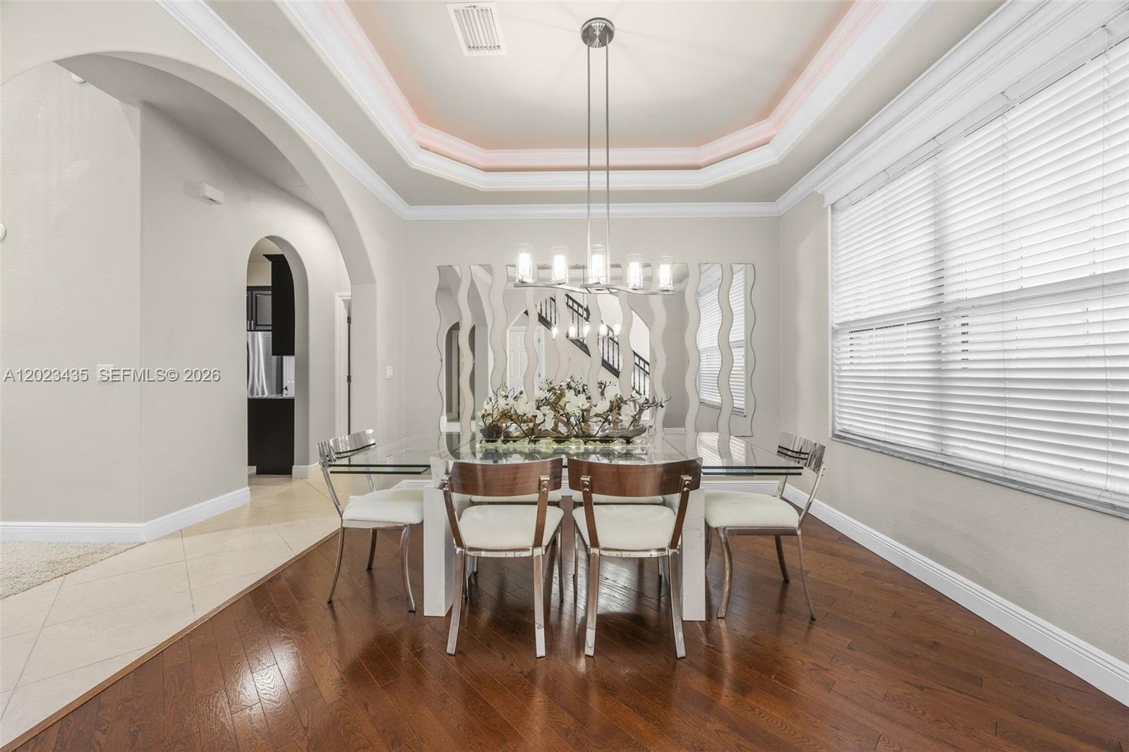 A dining room features a glass table, modern chairs, a tray ceiling, and hardwood floors — 14832 INDIGO LAKES CIR, Naples FL 34119, NAPLES, FL